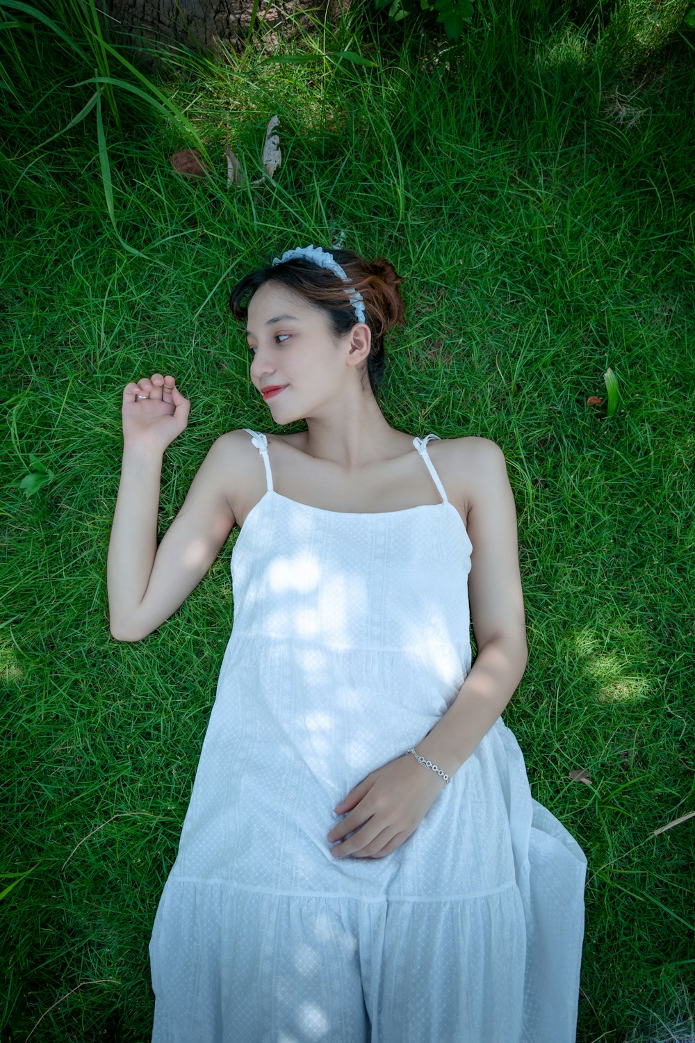 woman in white spaghetti strap dress lying on green grass field during daytime