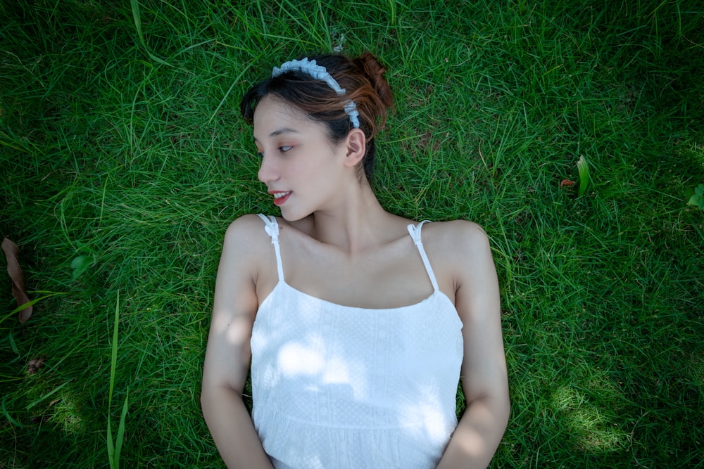 woman in white spaghetti strap top lying on green grass field during daytime