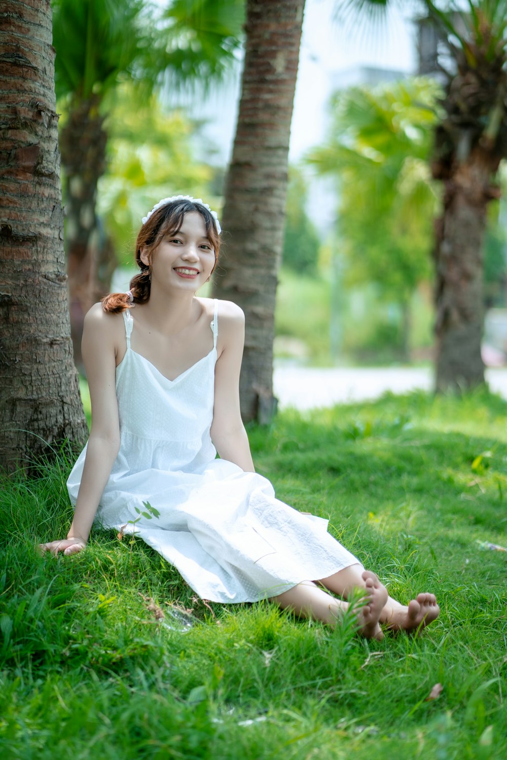 woman in white spaghetti strap dress leaning on tree