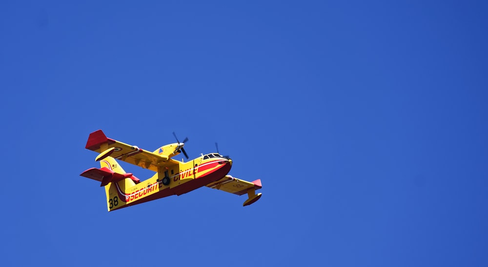 red and yellow plane flying under blue sky during daytime