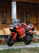red and black sports bike parked beside brown wooden door