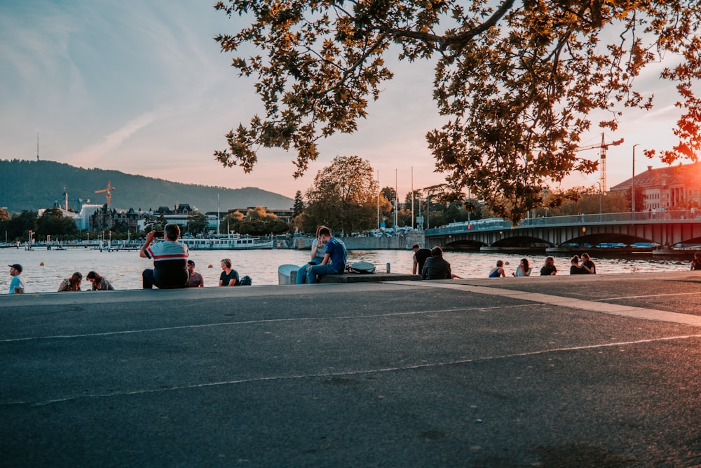 people sitting on gray concrete road near body of water during daytime