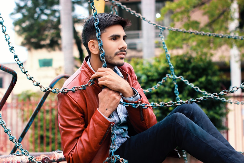 man in red leather jacket sitting on swing during daytime