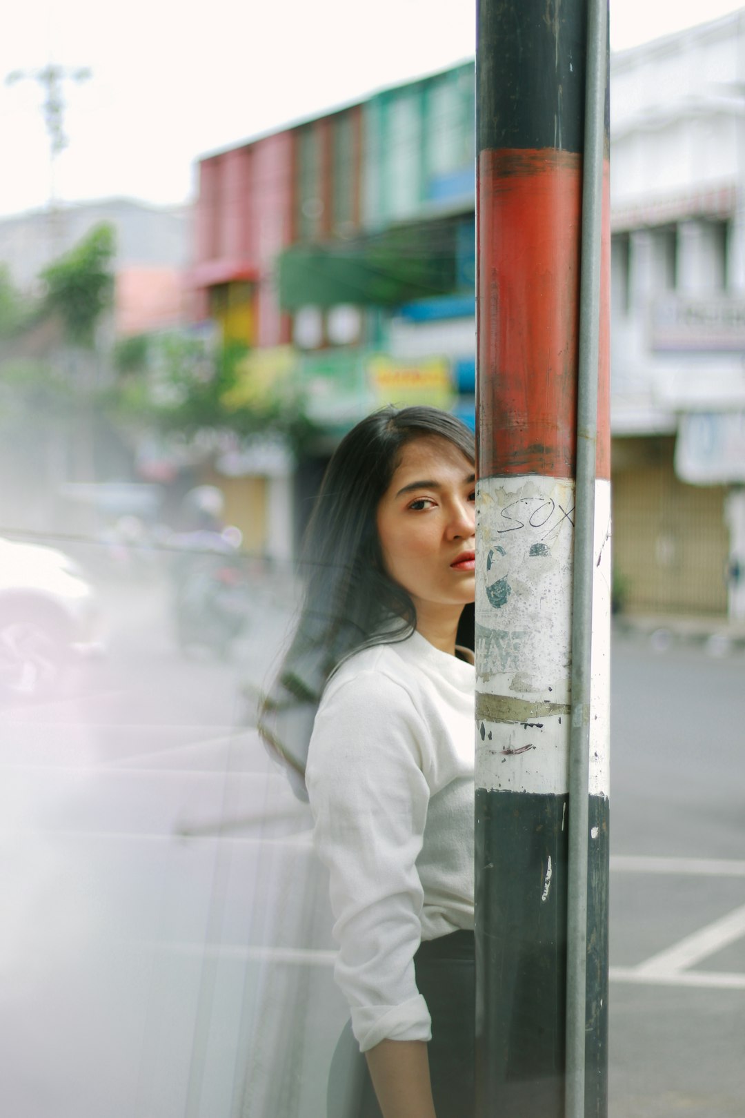 woman in white long sleeve shirt standing beside red metal post