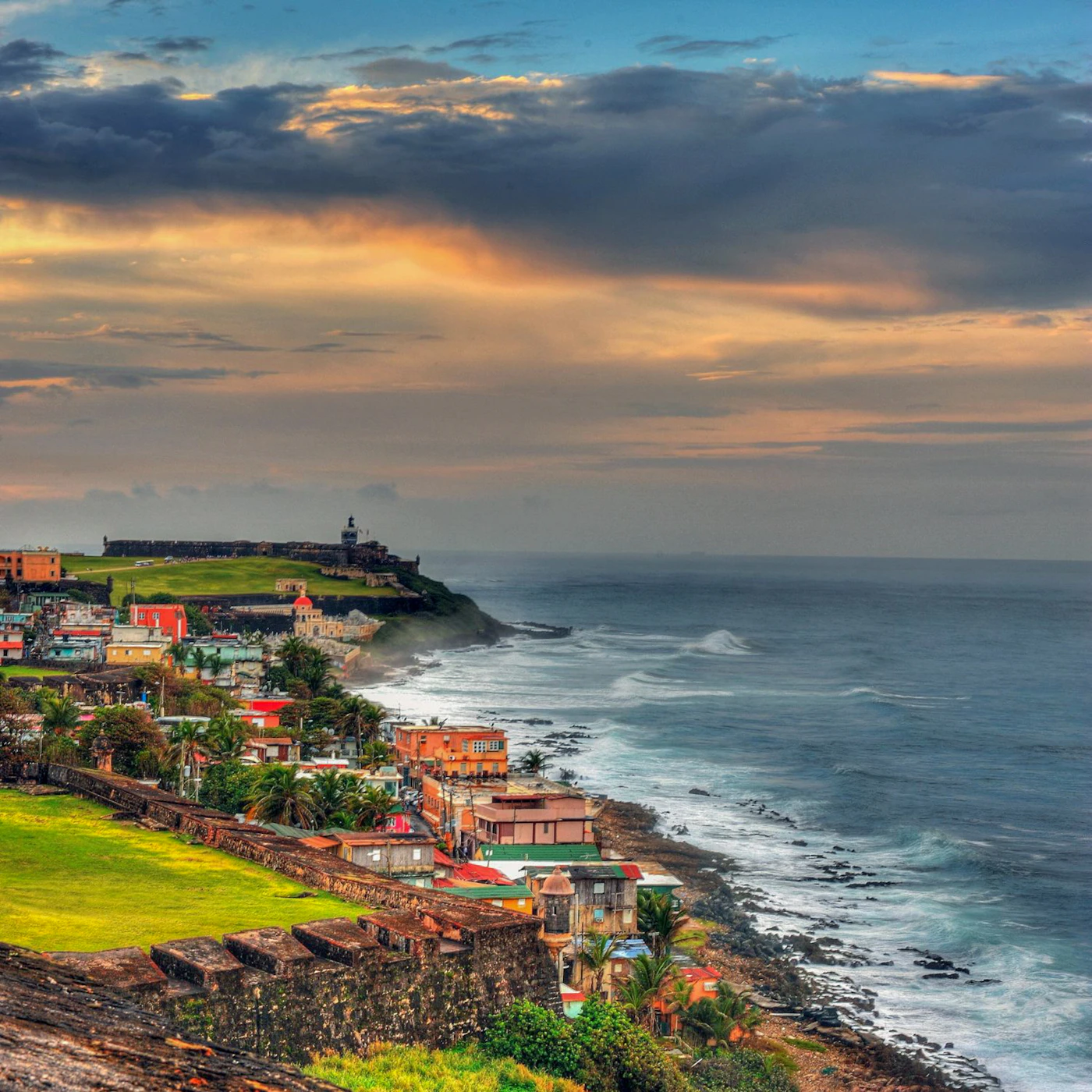 The colourful painted buildings of Old San Juan Puerto Rico with the iconic El Morro fortress visible above the town and the turquoise Atlantic visible behind the pastel blue and yellow facades
