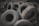 A pile of worn-out tires with various tread patterns stacked in an outdoor setting, surrounded by rocks and debris. The tires appear used and are arranged haphazardly.