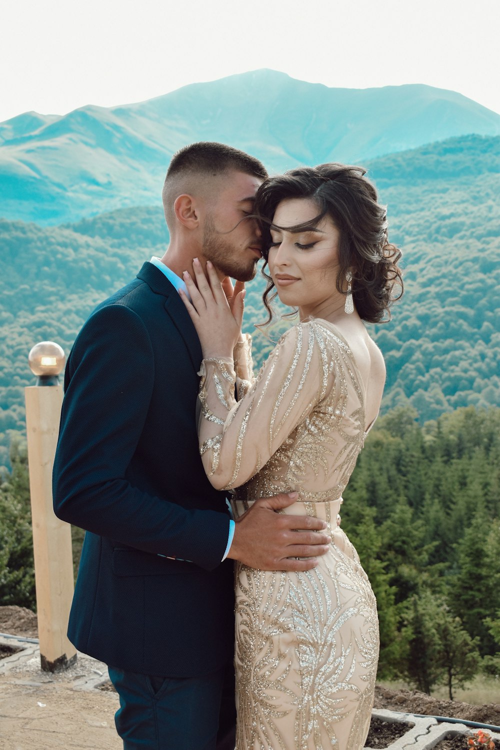 man in blue suit kissing woman in white lace dress