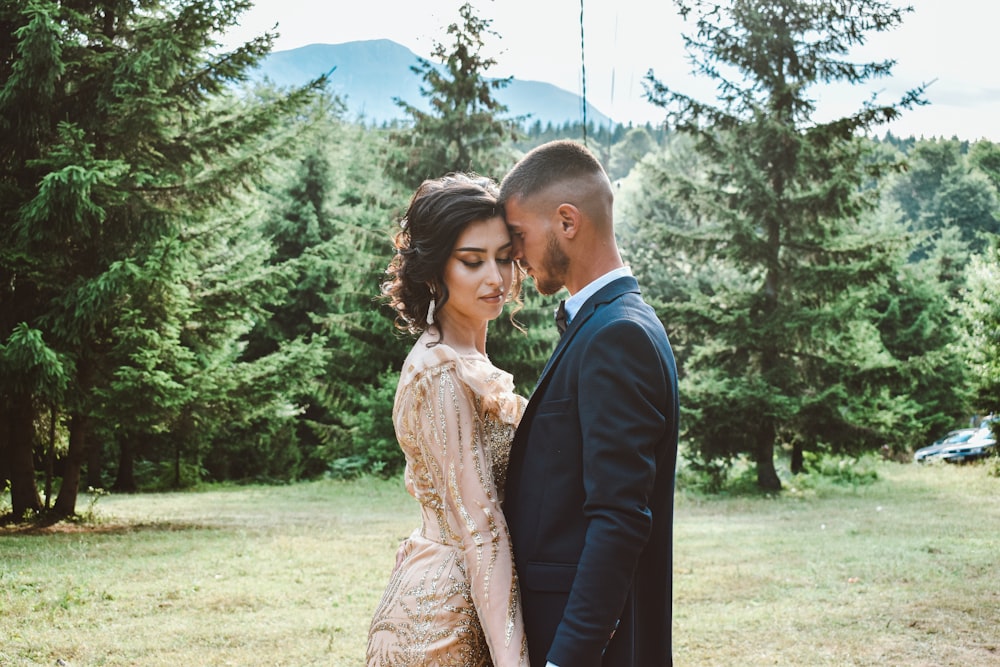 man in black suit jacket kissing woman in brown dress on green grass field during daytime