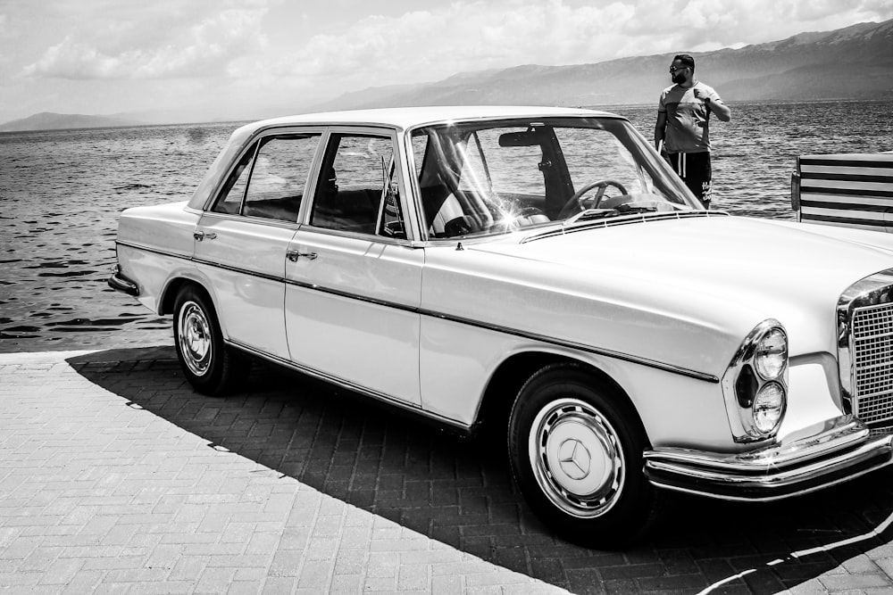 grayscale photo of man standing beside classic car