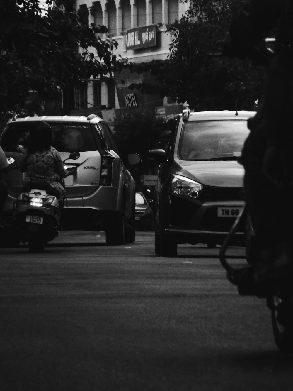 grayscale photo of man in black jacket and pants sitting on car hood