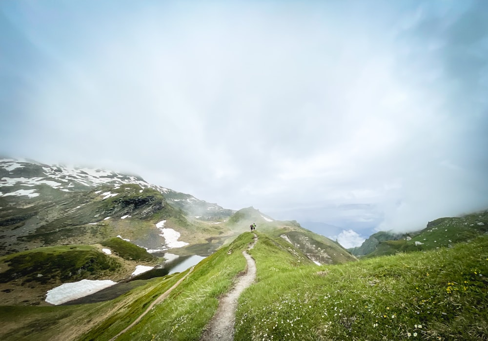 green grass field near mountain under white clouds during daytime