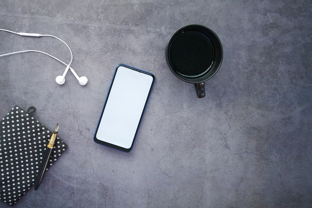 white iphone 5 c beside black round frame, top view of smart phone and notepad on table .