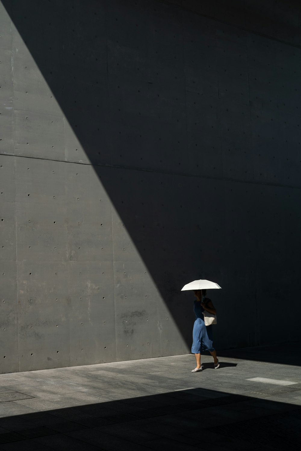 woman in white shirt and black pants holding umbrella walking on sidewalk during daytime