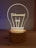 A wooden base supports an acrylic light resembling a lightbulb with the word 'Filament' inscribed on it. The design is softly illuminated, creating a warm, cozy glow.