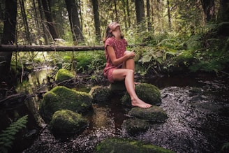 woman in purple and black floral dress sitting on rock in river