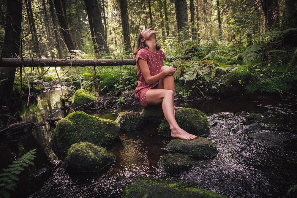 woman in purple and black floral dress sitting on rock in river