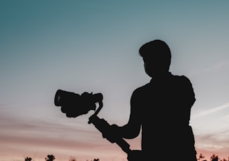 silhouette of man holding camera during sunset