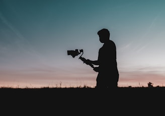 silhouette of man holding camera during sunset