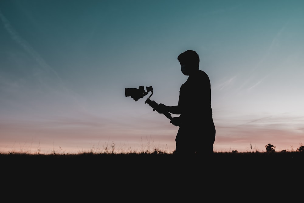 silhouette di uomo che tiene la macchina fotografica durante il tramonto