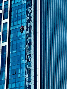 A professional cleaner using warm osmotic water to wash a large glass facade on a sunny day