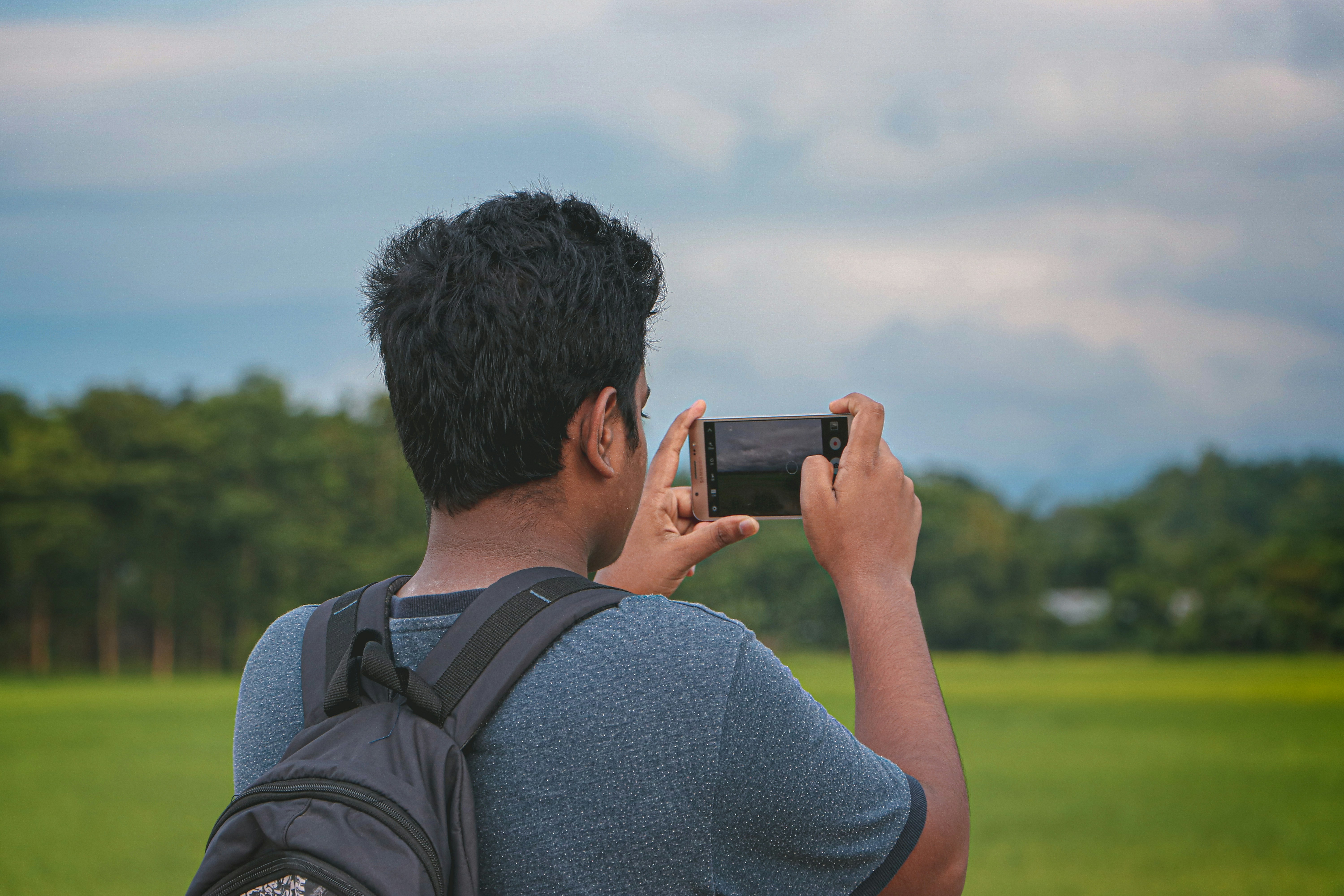 man in gray shirt holding black smartphone