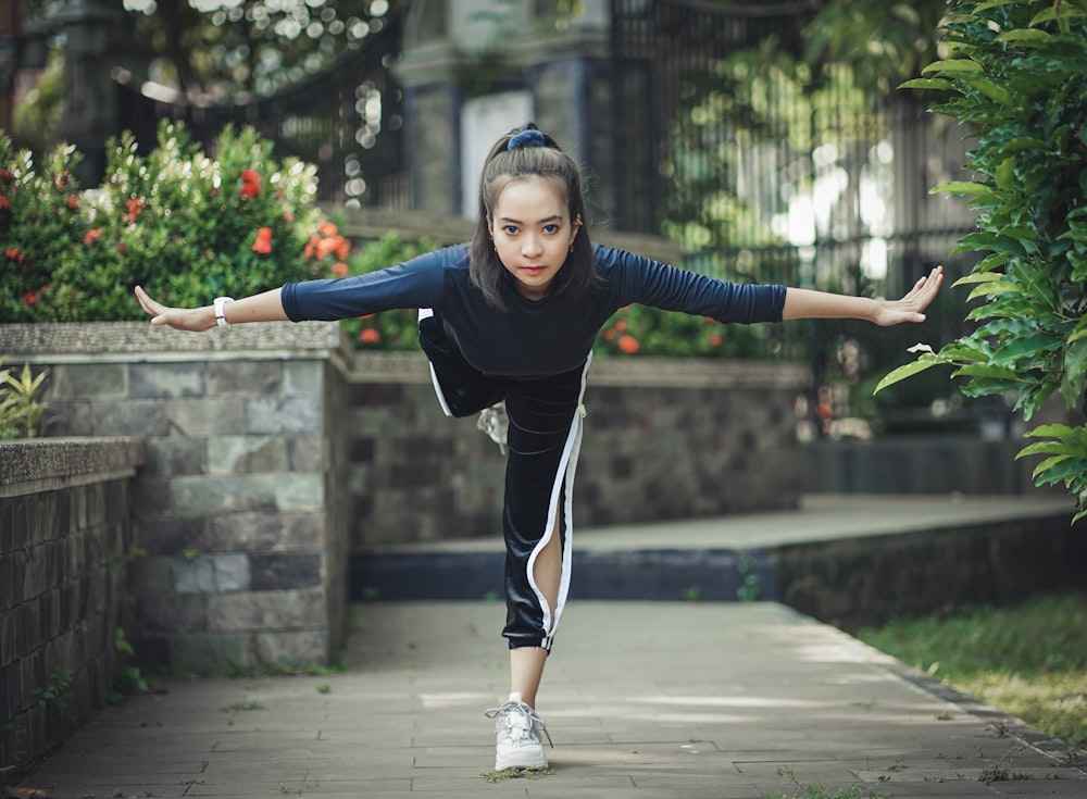 woman in black long sleeve shirt and black and white track pants standing on gray concrete