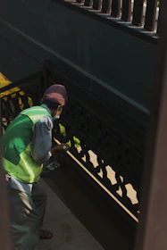 Close-up of hands cleaning a stair railing inside a residential building, emphasizing care and detail.