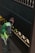A person wearing a green vest and a brown hat appears to be cleaning or painting a darkly-colored railing on a staircase. The light creates shadows on the walls, and the person is holding a small object in their hand.