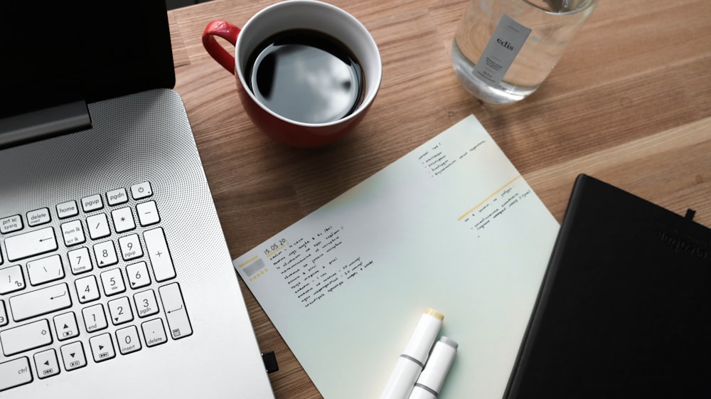 papier d’imprimante blanc à côté d’une tasse en céramique blanche sur une table en bois brun