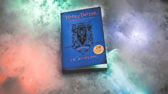A blue book with the title 'Harry Potter and the Philosopher's Stone' by J.K. Rowling is placed on a colorful, cloud-like background. The book cover features a crest and the word 'Ravenclaw'. A gold emblem marks the 20th anniversary of the book release.