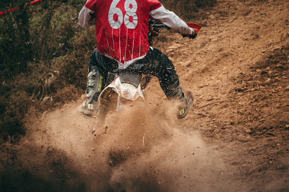 person in red and white long sleeve shirt and black pants running on brown dirt road