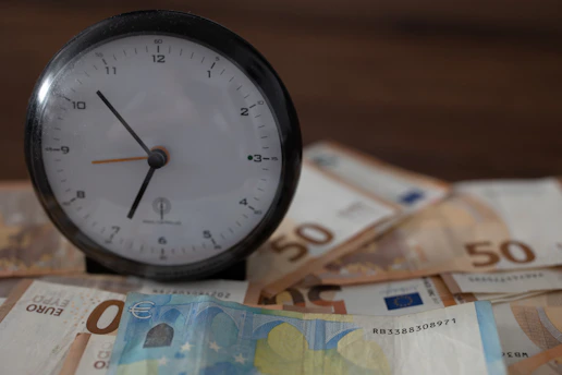 A close-up of a vintage clock and scattered financial newspapers on a wooden desk, symbolizing the passage of time in finance.