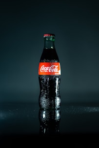 A chilled glass bottle of classic soda with condensation droplets, set against a circus-themed backdrop.