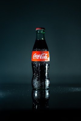 A chilled glass bottle of classic soda with condensation droplets, set against a circus-themed backdrop.