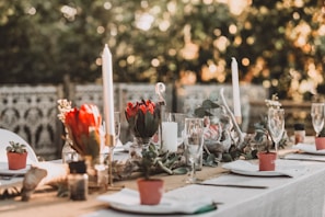 Elegant outdoor wedding table set with deep red flowers and satin cream linens under soft evening light