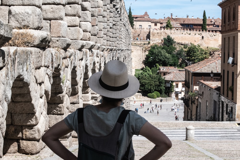 woman in blue crew neck t-shirt and brown fedora hat standing near brown concrete building