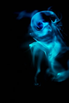 A swirling, ghostly blue smoke formation against a black background. The smoke appears ethereal, creating abstract and intricate patterns as it swirls and disperses.