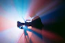 A person filming with a camera on a tripod in blue and red light