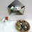 A metal envelope-shaped wall organizer holds several colorful cartoon-themed cards. Below it, a small white container holds red and brown markers next to a few sheets of white paper. A wicker basket contains painted stones with letters on them, arranged neatly.