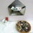 A metal envelope-shaped wall organizer holds several colorful cartoon-themed cards. Below it, a small white container holds red and brown markers next to a few sheets of white paper. A wicker basket contains painted stones with letters on them, arranged neatly.