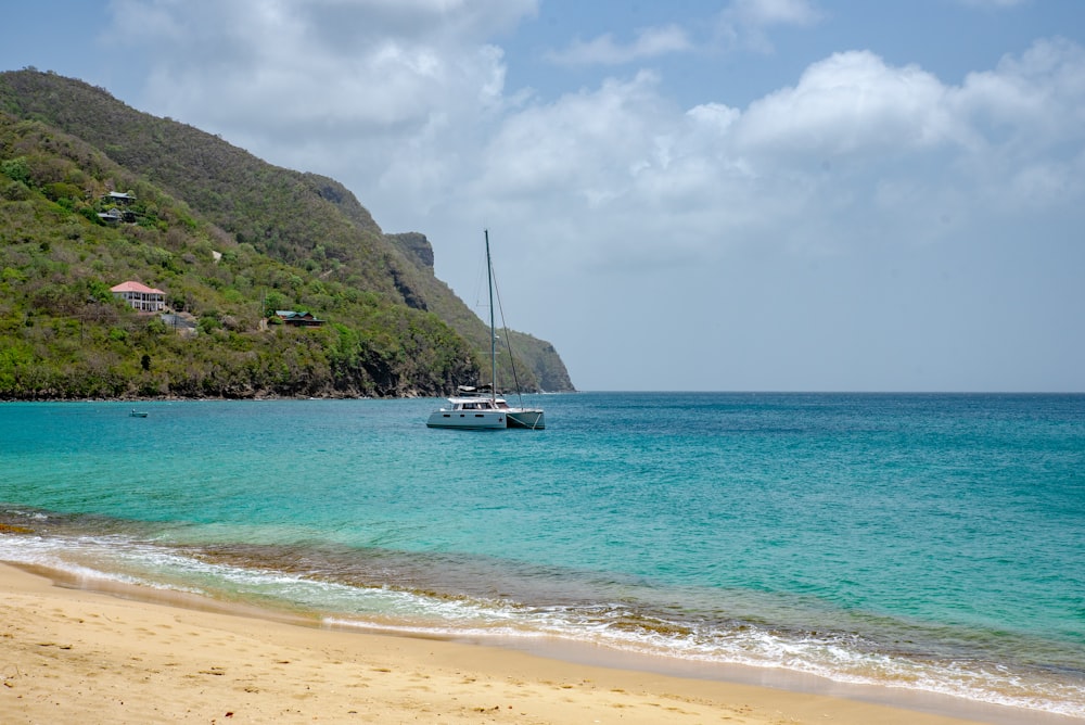 white boat on sea near green mountain under white clouds and blue sky during daytime