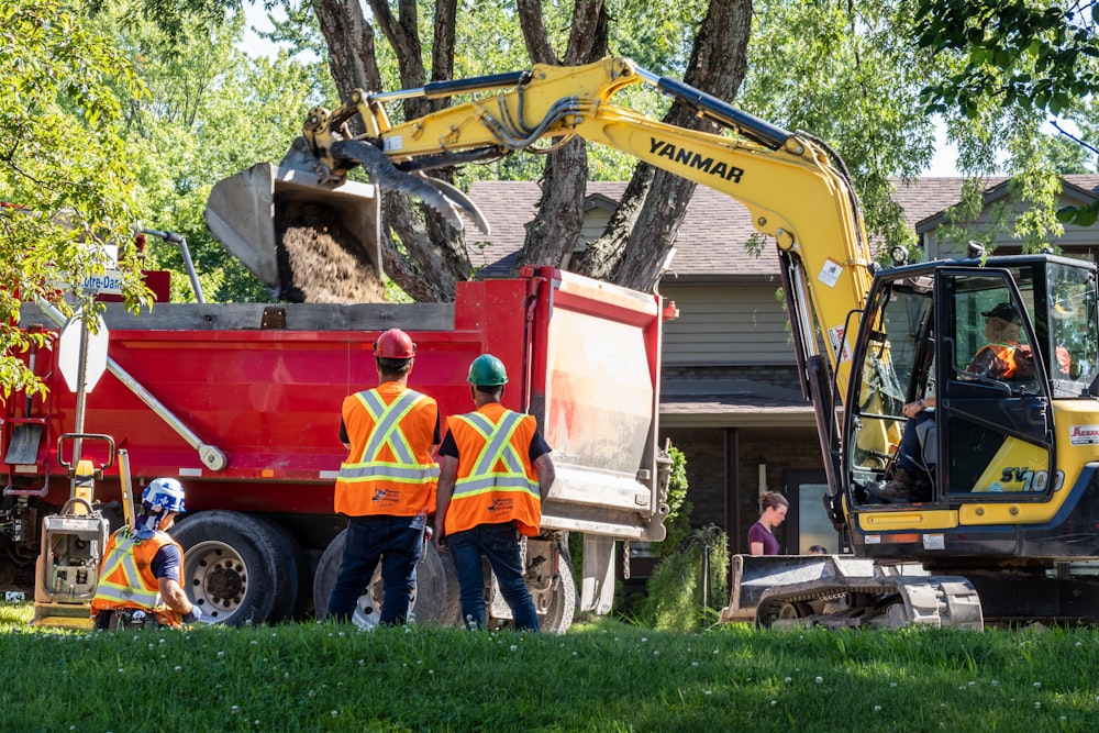 man in red and yellow jacket standing beside yellow and black excavator