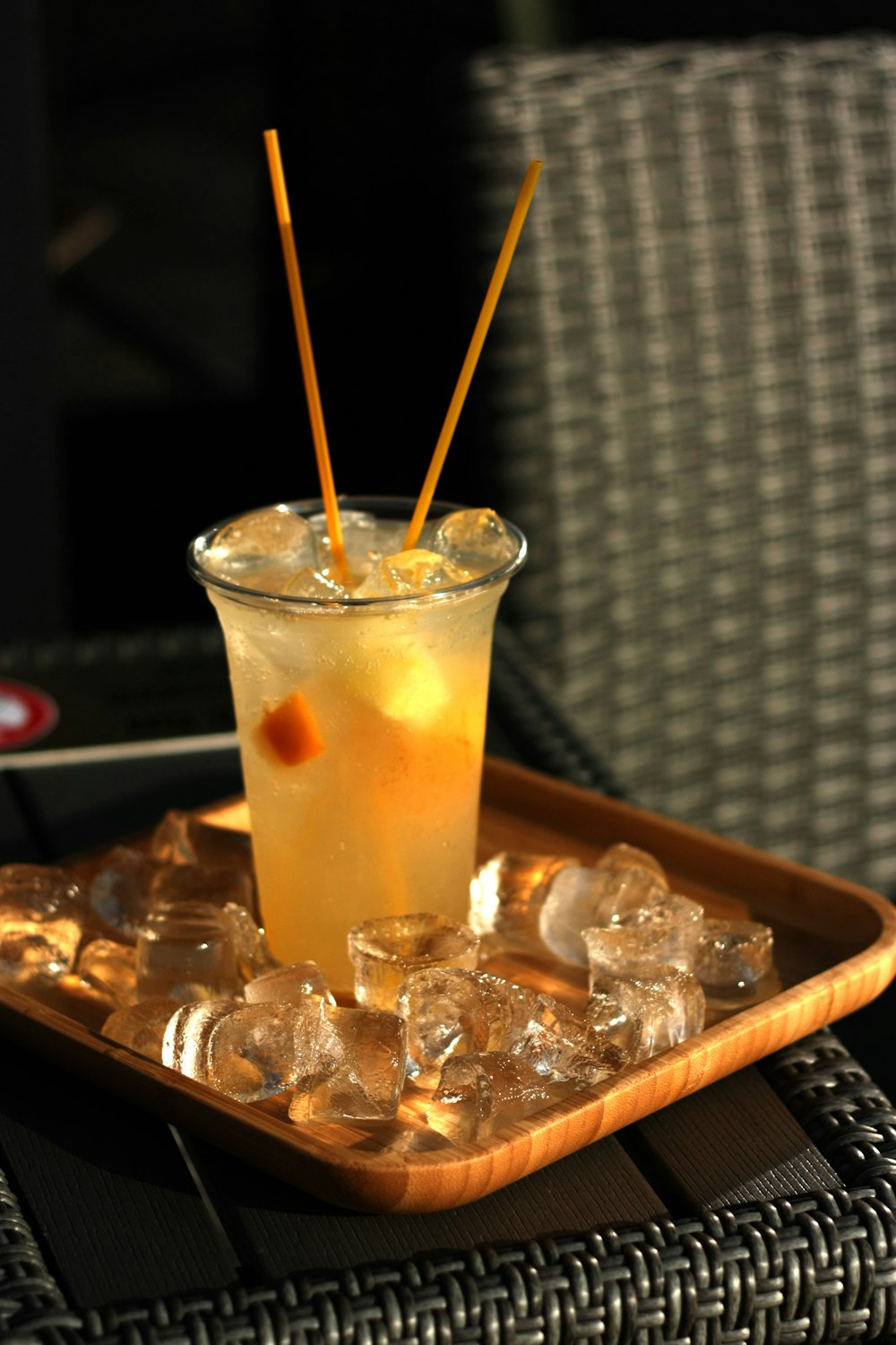 clear drinking glass with yellow liquid and ice cubes on brown wooden tray