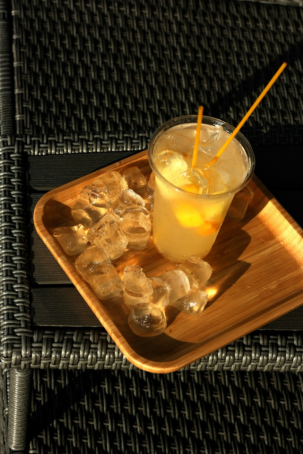 clear drinking glass with yellow liquid on brown wooden tray