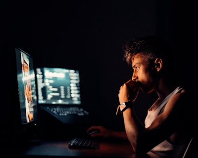 A person analyzing data on multiple monitors in a dark room.