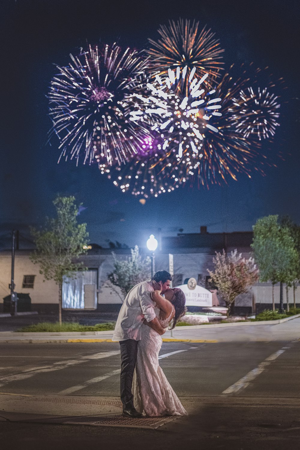 man in white dress shirt standing near pink and white fireworks during night time