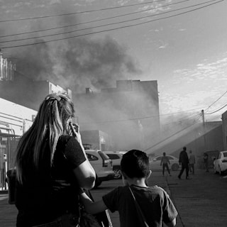 A poignant black-and-white photograph depicting displaced Palestinian families during the 1948 Nakba, carrying their few belongings amidst ruins.