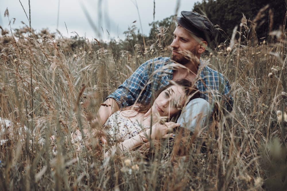 man in blue and white plaid button up shirt hugging woman in brown and green grass