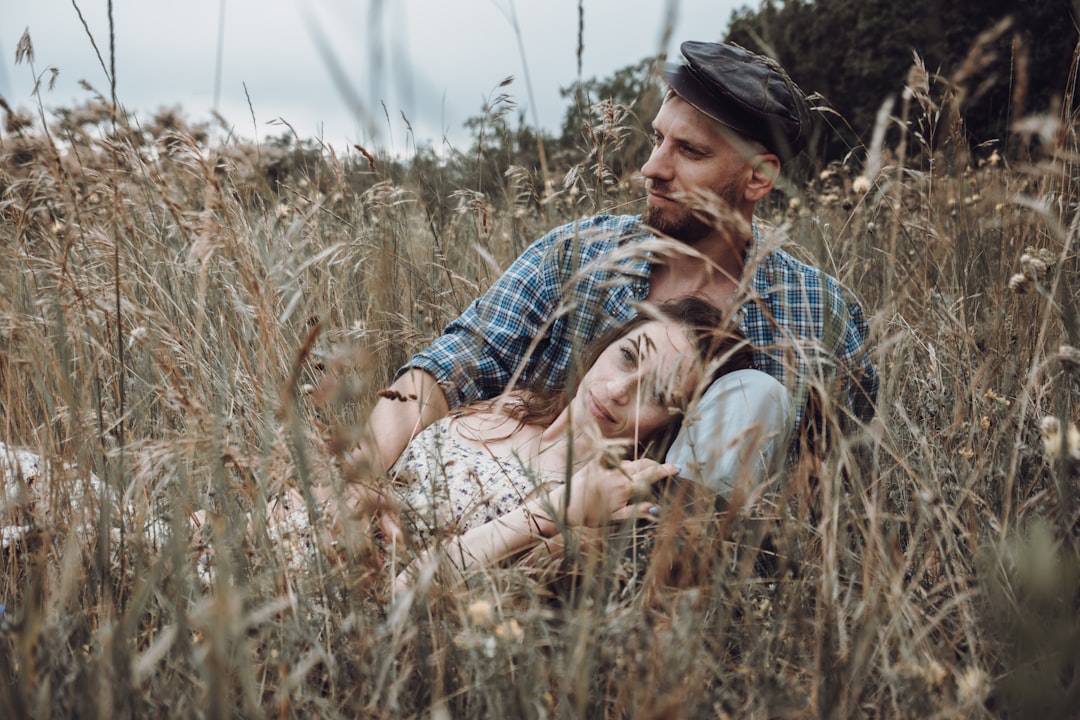 man in blue and white plaid button up shirt hugging woman in brown and green grass