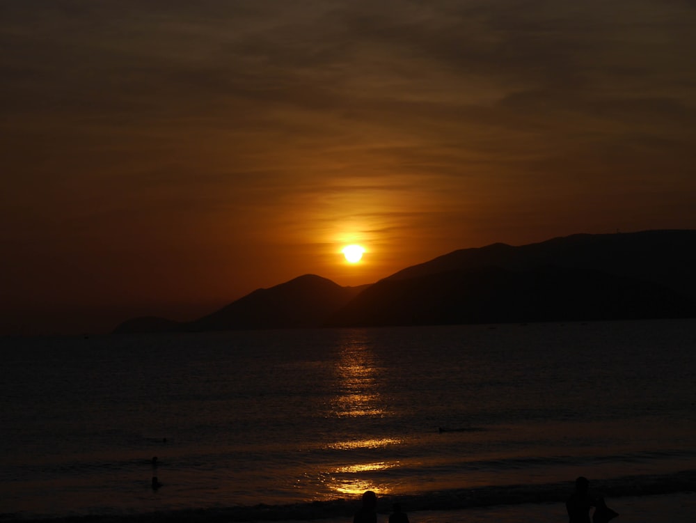 silhouette of people standing on beach during sunset